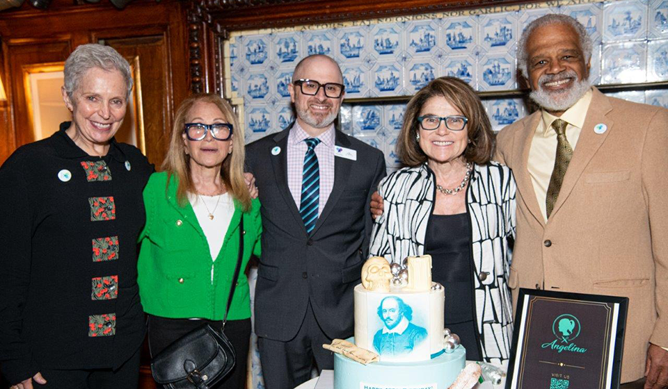 Group of people standing around a cake decorated with Shakespeare's portrait
