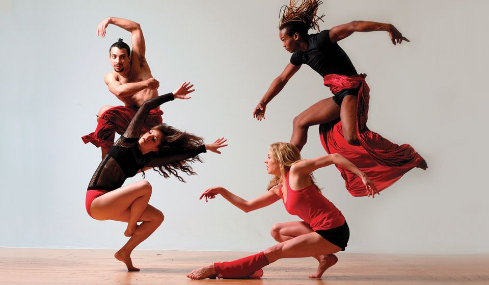 Four dancers in the middle of a routine. Two of them are in midair, the others crouched low.