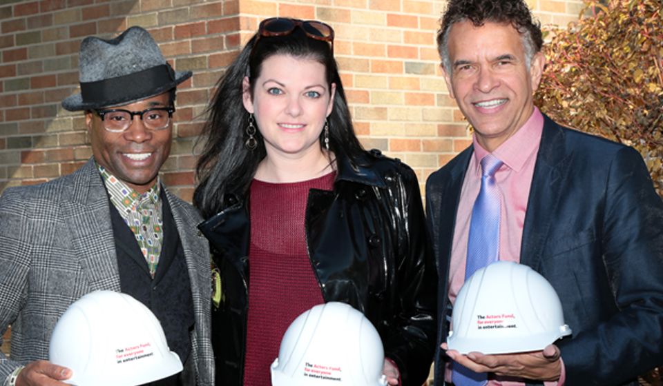 Three people holding hard hats in front of a brick wall