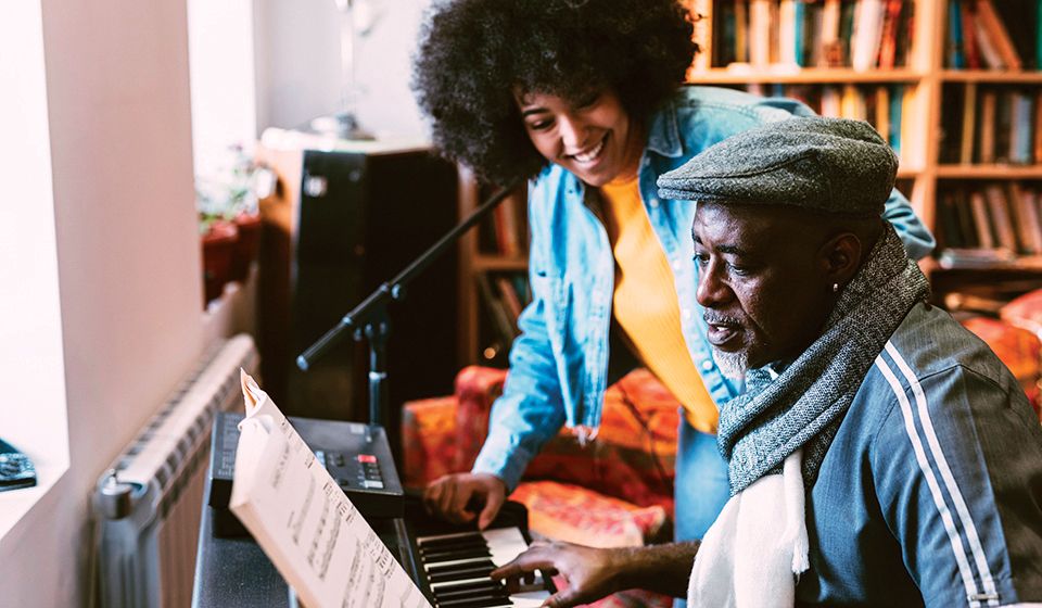 A man sits at a piano while a woman stands over him, smiling.