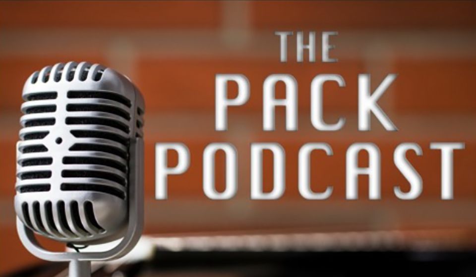 Close-up of a microphone in front of a brick wall. To the right, the words "the Pack Podcast"