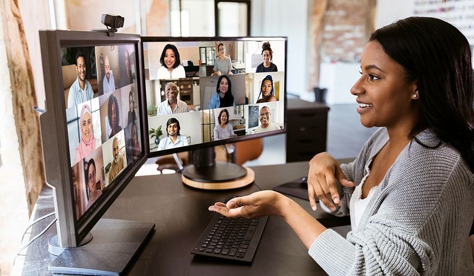Woman making a presentation on a videoconference, with multiple faces on her computer screens.