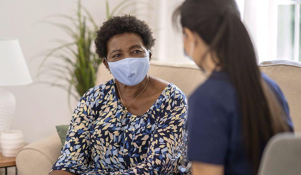 An older woman wearing a facemask speaking with a healthcare professional